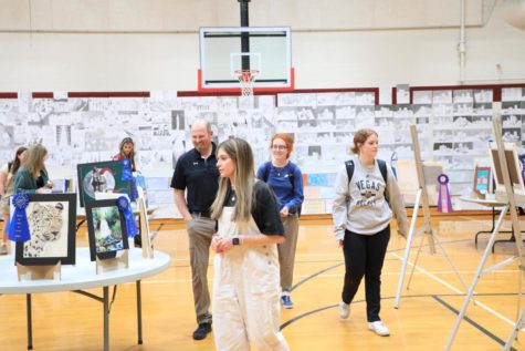 ARTSY: Students peruse the art on display in the auxiliary gym. Amongst the art on display were the pieces awarded ribbons at the state art symposium. Trinity Roberson—pictured here behind Mr. Lancaster, Morgan Scaffide, and Loren Erickson—submitted art that was recognized in the top 25 of over 2000 entries. 