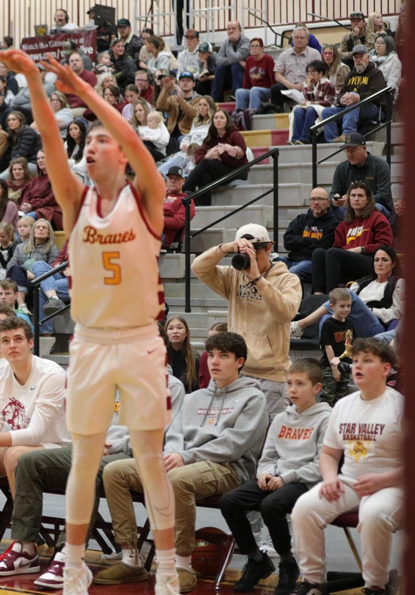 Dylan Shumway puts up a shot against Kelly Walsh as elementary student and bench guest looks on from the far right of the photo. The kid also got to join the team on the bench as well the locker rooms pre-game and at half time. He also snagged Braves Merch like a  Star Valley Braves t- shirt and a mini basket ball signed by each player.